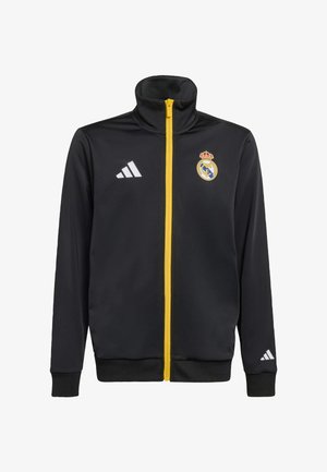 Musta urheilutakki, jossa on korkea kaulus, keltainen vetoketju ja valkoinen Adidas-logo. Rintakehässä Real Madridin tunnus.