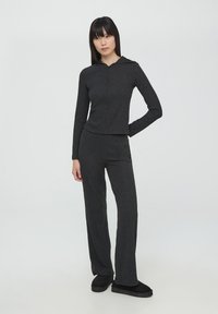 Maglione grigio a coste con cappuccio e zip, abbinato a pantaloni a zampa coordinati. Il materiale è morbido con un aspetto leggermente strutturato. Calzature nere.