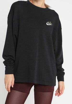 Femme portant un sweat-shirt noir surdimensionné avec un petit logo Nike et un short moulant bordeaux, sur un fond uni.