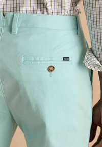 Világos türkiz pamutnadrág sima textúrával. Hátul egy zseb található gombbal és egy kis "Joules" márkacímkével.