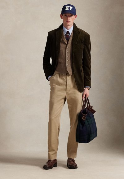 Καφέ σακάκι από κορδόνι, μπεζ παντελόνια, καφέ γιλέκο με υφή, ριγέ πουκάμισο και μπλε καπέλο NY. Καφέ παπούτσια και σκούρα τσάντα με καρό σχέδιο.
