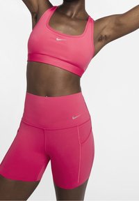 Różowy sportowy stanik i szorty o wysokim stanie, wykonane z gładkiego materiału, z małym srebrnym logo Nike z przodu.
