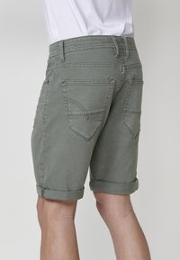 Shorts en coton vert olive avec revers, dotés de deux poches arrière et d'une ceinture visible, conçus avec des détails piqués.