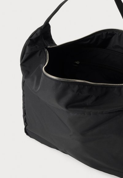 Sac à épaule en tissu noir avec une large ouverture zippée, montrant un intérieur spacieux et une seule bandoulière.