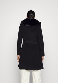 Černý kabát s límcem z umělé kožešiny, přizpůsobený design, střední délka, dvě zadní knoflíky a boční kapsy, s hladkou texturou.