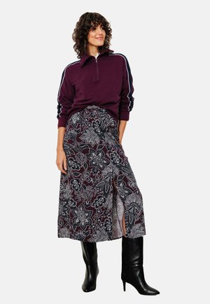 Sweatshirt bordeaux zippé avec des rayures blanches, associé à une jupe maxi à motifs floraux noir et blanc, et des bottes noires à talons hauts.