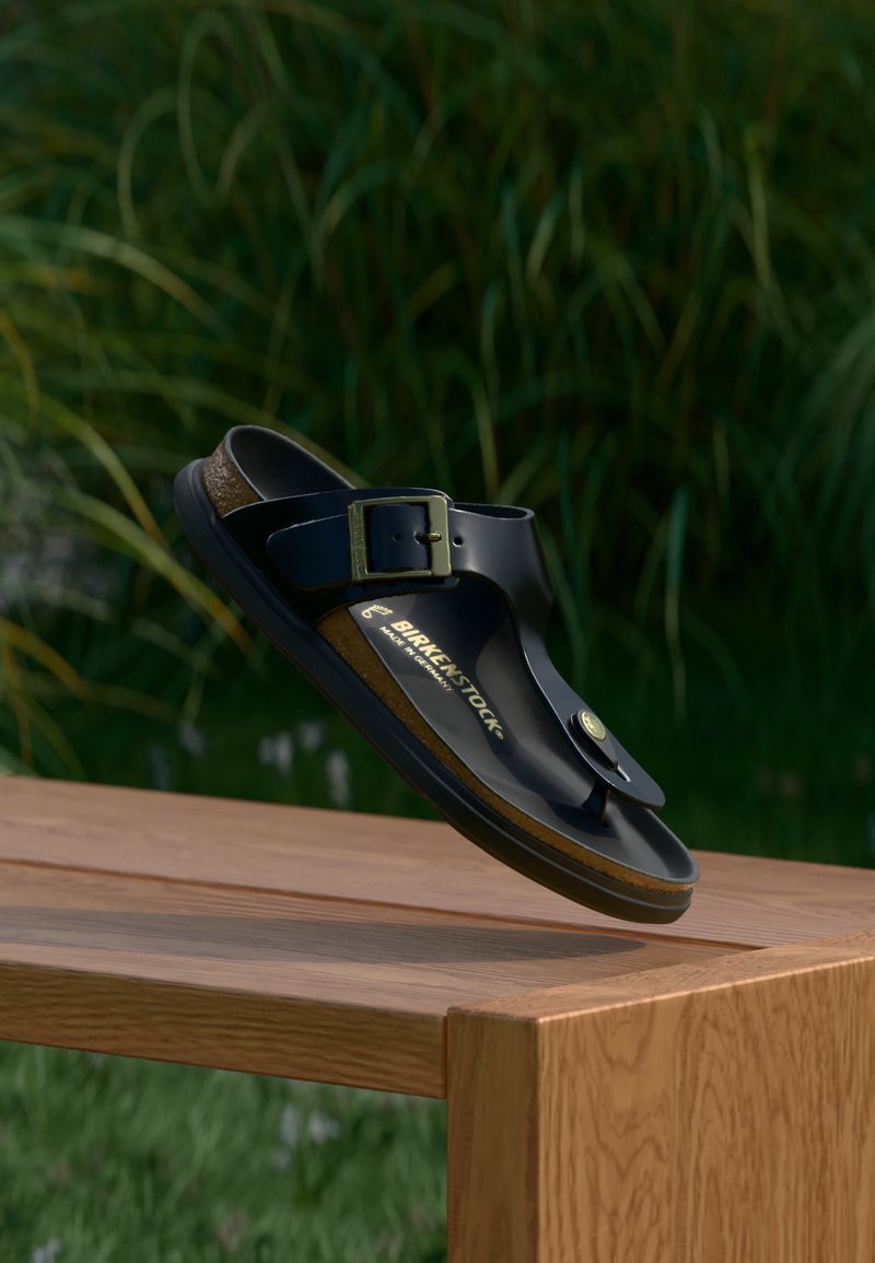 Μαύρο σανδάλι Birkenstock με αγκράφα που ακουμπά σε ξύλινο τραπέζι σε εξωτερικό χώρο με θολωμένα πράσινα φυτά στο φόντο.