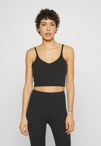 Top corto negro con tirantes finos, escote en V, hecho de una tela suave. Combinado con leggins negros de tiro alto, ambos en una textura lisa.