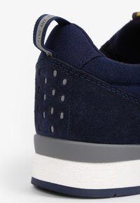 Marineblauwe sneaker met een combinatie van suede en mesh materialen, een gestructureerde grijze zool en een trekband met logo-detail.