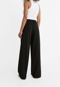 Pantalon noir à jambes larges avec une taille élastique, fabriqué en tissu lisse, doté d'une coupe décontractée sans motifs ni accessoires visibles.