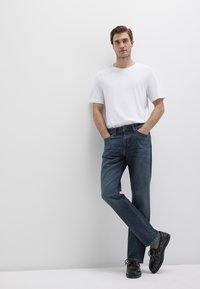 White cotton T-shirt paired with dark blue denim jeans. Black sneakers with laces. Casual fit, standing pose against a plain background.