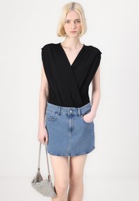 Top negro con mangas cortas, combinado con una falda de mezclilla azul claro con bolsillos y un bolso plateado. Diseño simple y moderno.