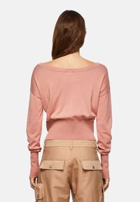 Różowa bluzka z długim rękawem, odkrytymi ramionami, wykonana z miękkiego dzianiny. Ma dopasowaną talię i luźne rękawy. Połączona z beżowymi spodniami typu cargo z bocznymi kieszeniami.