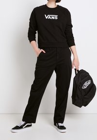 Felpa nera corta con logo bianco "VANS", pantaloni neri e zaino Vans nero. Calzature: sneakers nere con dettagli bianchi.