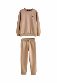 Beige pitkähihaisuus huppari, jossa on pieni dinosauruksen logo rinnassa, yhdistettynä samasta materiaalista valmistettuihin joustavyötäröisiin jogging-housuihin.