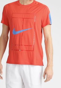 Röd atletisk t-shirt med korta ärmar, med en blå Nike-logotyp och en glänsande rektangulär design på framsidan.