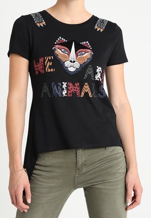 Chemise noire à manches courtes avec visage de lion coloré brodé et texte "NOUS SOMMES DES ANIMAUX", portée avec un pantalon vert olive.