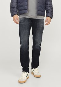 Temno modri jeans s ožjim krojem, z blagim vintage učinkom, dokončane hlačnice in vidnim šivanjem. Ujemajo se z belimi supergami.