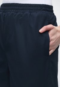 Χέρι τοποθετημένο στην μπροστινή τσέπη ενός μαύρου, ελαστικού, καθημερινού παντελονιού, φορεμένου με λευκό τοπ.