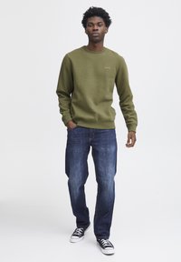 Olijfgroene sweatshirt met een ronde hals en subtiele "blend" logo, gecombineerd met blauwe denim jeans en zwarte sneakers. Klassieke casual pasvorm.