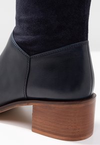 Svart läder och marinblå mocka ankelskor med träblockklack. Har en slät finish och kontrasterande texturer vid ankeln.