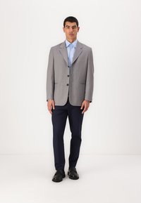 Grå blazer med slagkrage, två knappar och fickor med lock, tillsammans med en ljusblå skjorta och navybyxor, kompletterad med svarta skor.