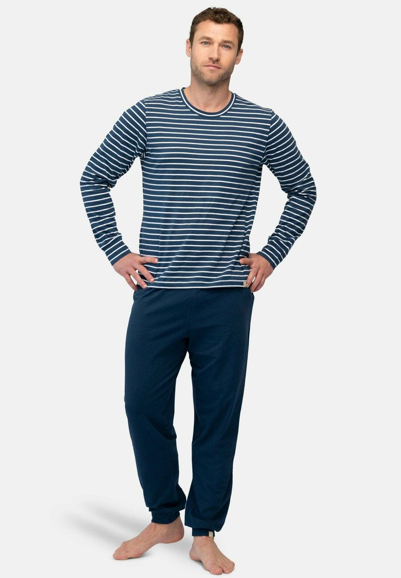 Marineblauwe en witte gestreepte blouse met lange mouwen, gecombineerd met effen marineblauwe broek. Katoenen stof, losse pasvorm, manchetjes aan de polsen en enkels met accent.