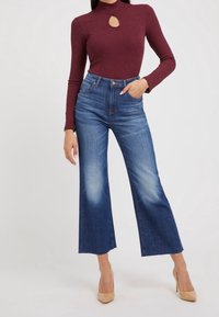 Bordeaux langharige top met een keyhole-detail, gecombineerd met hoog- Taille, wijde blauwe jeans met vervaagde delen en rauwe zomen.