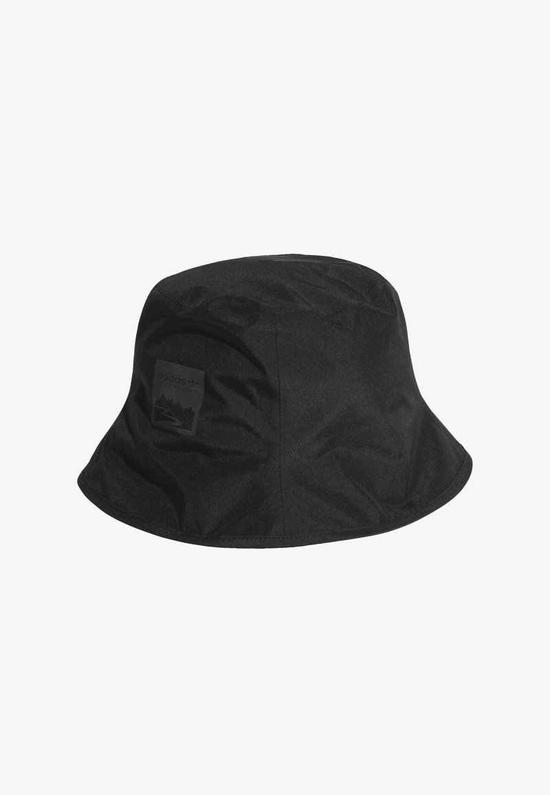 Melns buks ar plakanu vainagu, izgatavots no gludas auduma, ar plašu, uz leju slīpo malām. Iekļauts reljefs logotipa uzlīme sānos.