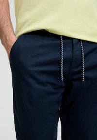 Granatowe spodnie z teksturowanej tkaniny, z bocznymi kieszeniami i elastycznym pasem ze sznurkiem, z czarnymi i białymi akcentami.