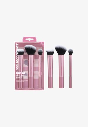 Trois pinceaux de maquillage roses avec des poils blancs et noirs dans un emballage transparent étiqueté "Real Techniques Peak Cheek Brush Set."