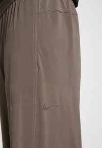Nike træningsbukser i dæmpet brun stof med en glat tekstur. Har elastisk talje, sidelomme og et reflekterende logo.