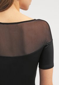 Černý body s průhlednou síťovanou zadní částí, krátkými rukávy a širokým výstřihem s pevným černým lemem podél okrajů.