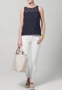 Granatowy top na ramiączkach z koronką i przezroczystymi panelami, zestawiony z białymi dopasowanymi dżinsami. Dodatki stanowią jasnobeżowa torebka i kolorowa bransoletka.