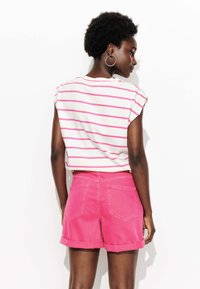 T-shirt blanc rayé avec des rayures roses, manches retroussées, associé à un short en denim rose avec des ourlets retroussés et des poches arrière.