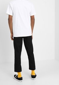 Vit bomull t-shirt, svarta byxor, gula strumpor och svarta sneakers. Enkelt mönster, rak passform, minimala accenter.