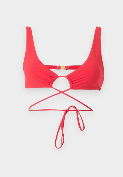 Κόκκινο τοπ μπικίνι με ρυθμιζόμενους δεσίμους που διασταυρώνονται μπροστά και μια μικρή χρυσή αγκράφα στο πίσω μέρος, εμφανίζεται σε απλό φόντο.