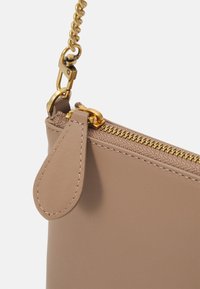 Beige leren zakje met een gouden metalen rits en hardware, met een gestructureerde accent nabij de rits en een haak voor een kettingriem.