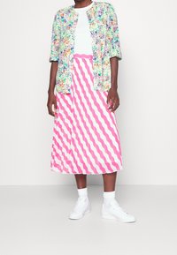 Veste à manches courtes colorée à motif floral portée sur un haut blanc et une jupe midi rose à rayures ondulées, assortie à des baskets blanches et des chaussettes.