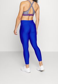 Niebieskie legginsy sportowe z wysokim pasem, wykonane z elastycznego materiału. Dopasowane do szarego biustonosza sportowego z krzyżującym się tyłem.