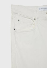 Gros plan sur un jean en denim blanc montrant la poche avant, la petite poche avec rivets métalliques et la passants de ceinture.