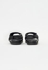 Sorte sandaler med strukturerte stropper, flate såler og et minimalistisk design. Har justerbare stenger og en jevn tekstur.