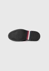 Semelle en caoutchouc noir avec des rainures horizontales, dotée d'une bande d'accent multicolore rouge, blanc et bleu. Fini lisse et texturé.