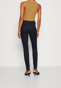 Vaqueros ajustados de mezclilla azul oscuro, con cintura media y bolsillos traseros, combinados con una blusa sin mangas de color canela.
