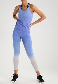Completo sportivo con gradiente blu composto da un top senza maniche e leggings con una transizione di colore sfumata dal blu scuro al blu chiaro. Calzature nere.
