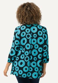 Zwarte tuniek met blauwe cirkelpatronen, voorzien van driekwart mouwen en een losse pasvorm, gemaakt van een gladde stof voor comfort.