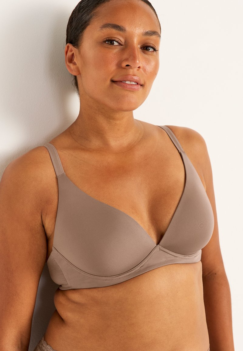 Vaaleanruskea rintaliivi, jossa on sileä ja joustava kangas. Siinä on V-muotoinen kupin muotoilu ja säädettävät olkaimet. Koristeluja ei ole näkyvissä.