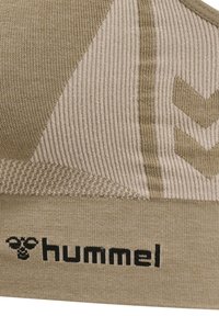 Beige idrotts-bh med ribbat mönster. Har en triangulär design, chevronmönster och svart "hummel"-logotyp vid bandet.