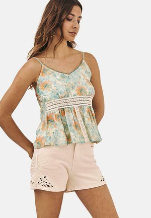 Top sin mangas ligero con un patrón floral en verde y naranja, con un borde de encaje en la cintura, combinado con pantalones cortos crema con bordados.