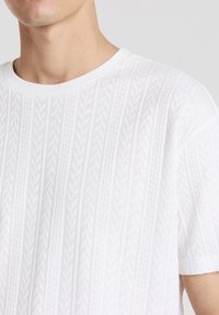 Maglione a maniche corte bianco in knit con un motivo testurizzato che ricorda l'iconico motivo herringbone, dotato di scollatura rotonda e una finitura morbida.